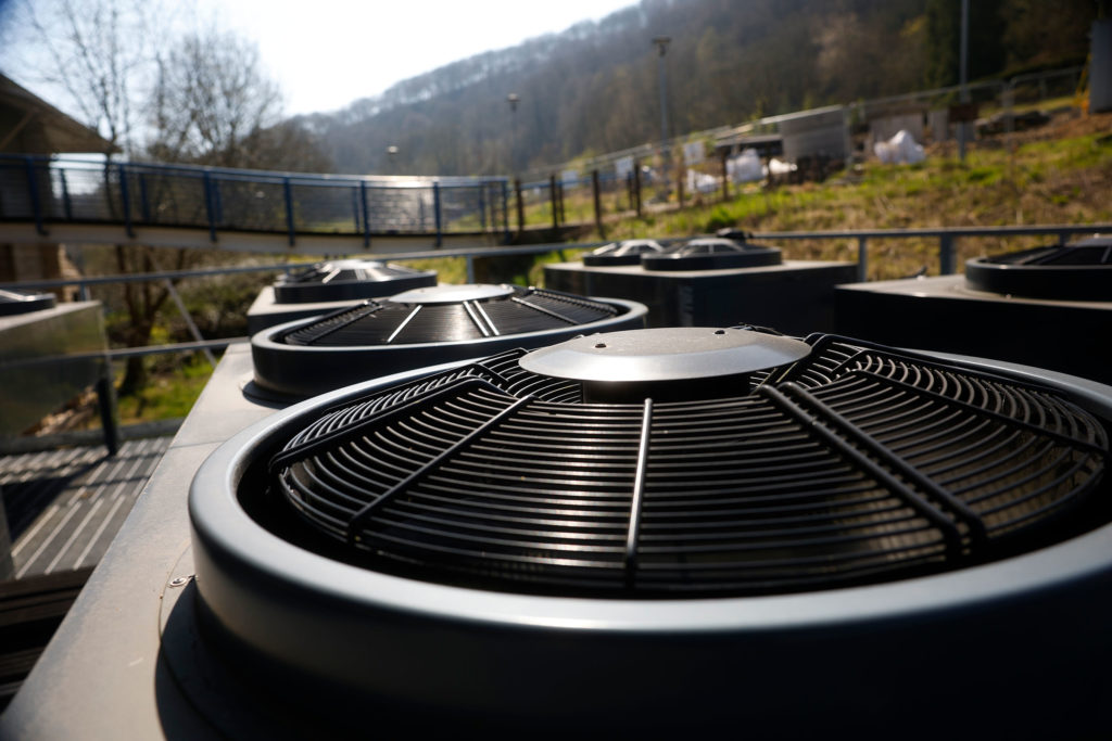 Close-up of a grey Ochsner commercial heat pump unit mounted on a raised steel mesh platform above the plant rooms at Todmorden Sports Centre.