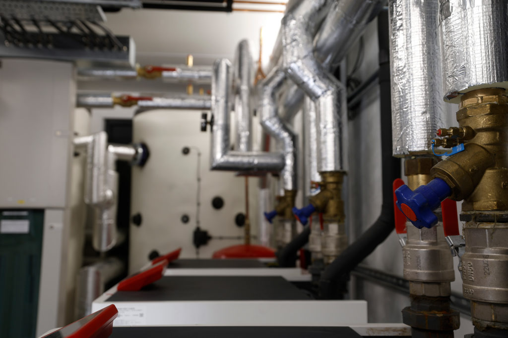 Interior of the commercial plant room at Todmorden Sports Centre showing indoor Ochsner heat pump modules, insulated pipework, and a 3,000-litre buffer tank.