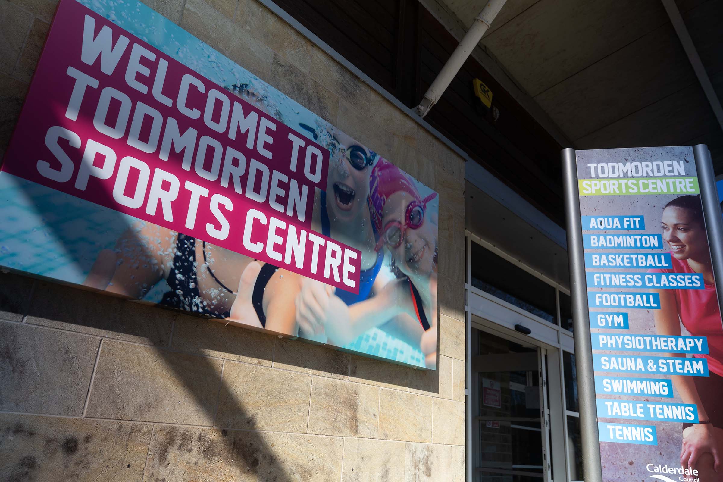 Front reception entrance and welcome sign at Todmorden Sports Centre in Calderdale on a sunny day.
