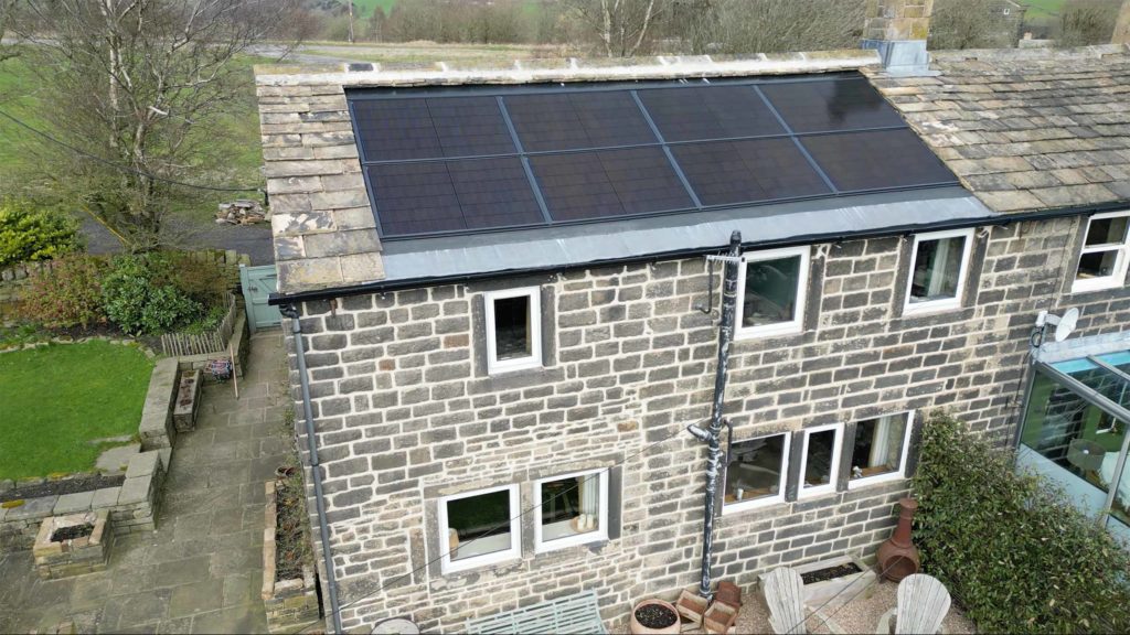 Aerial drone view of eight all-black in-roof solar panels integrated flush into a traditional Yorkshire stone slate cottage roof.