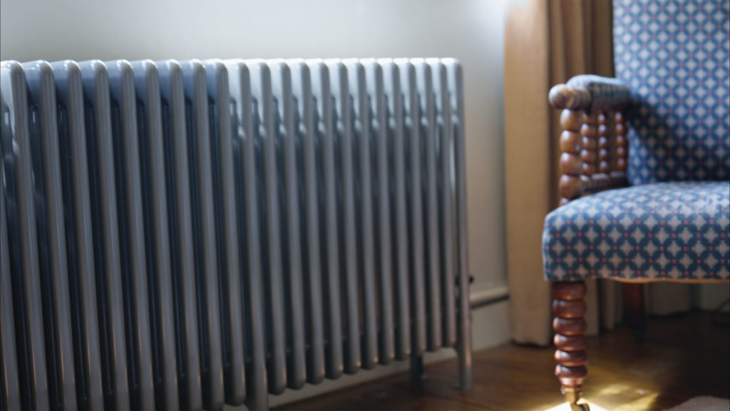 Traditional cast-iron style column radiator fitted beneath a cottage window next to an armchair in a Yorkshire stone home.