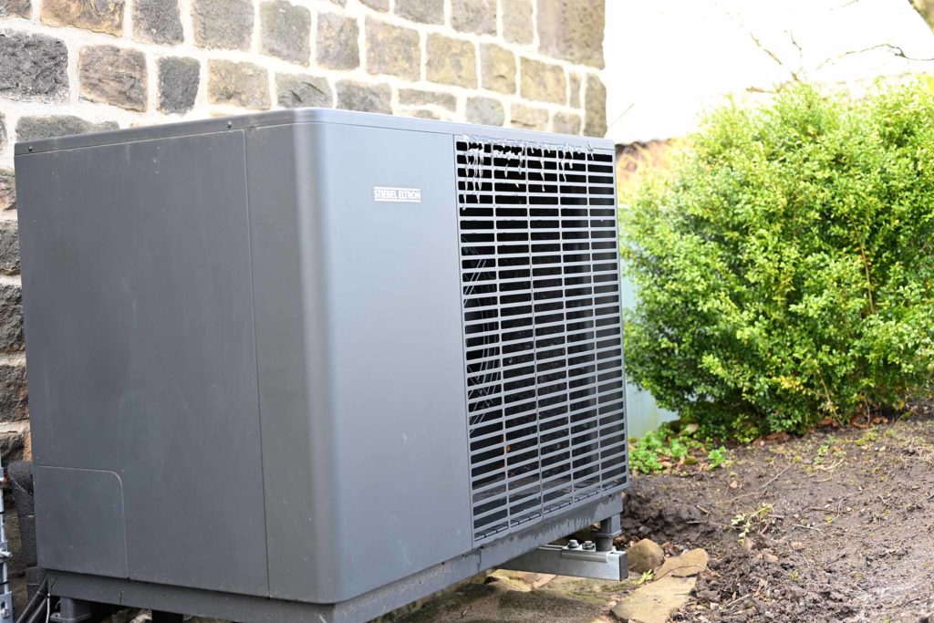 Dark grey Stiebel Eltron air source heat pump with winter icicles against a traditional Yorkshire stone garden wall.